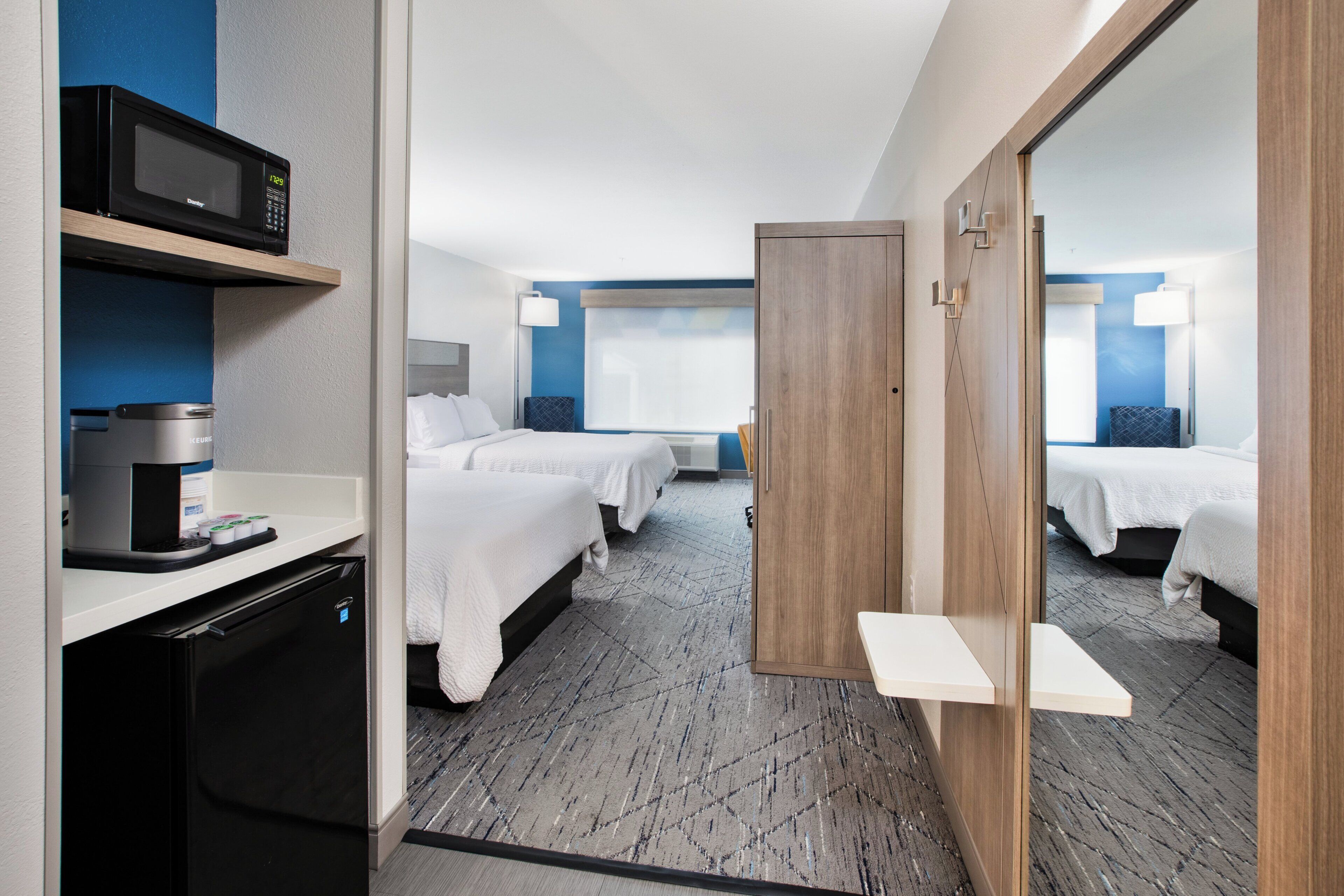 A hotel room with two beds, a kitchenette, and a mirror reflecting the room.