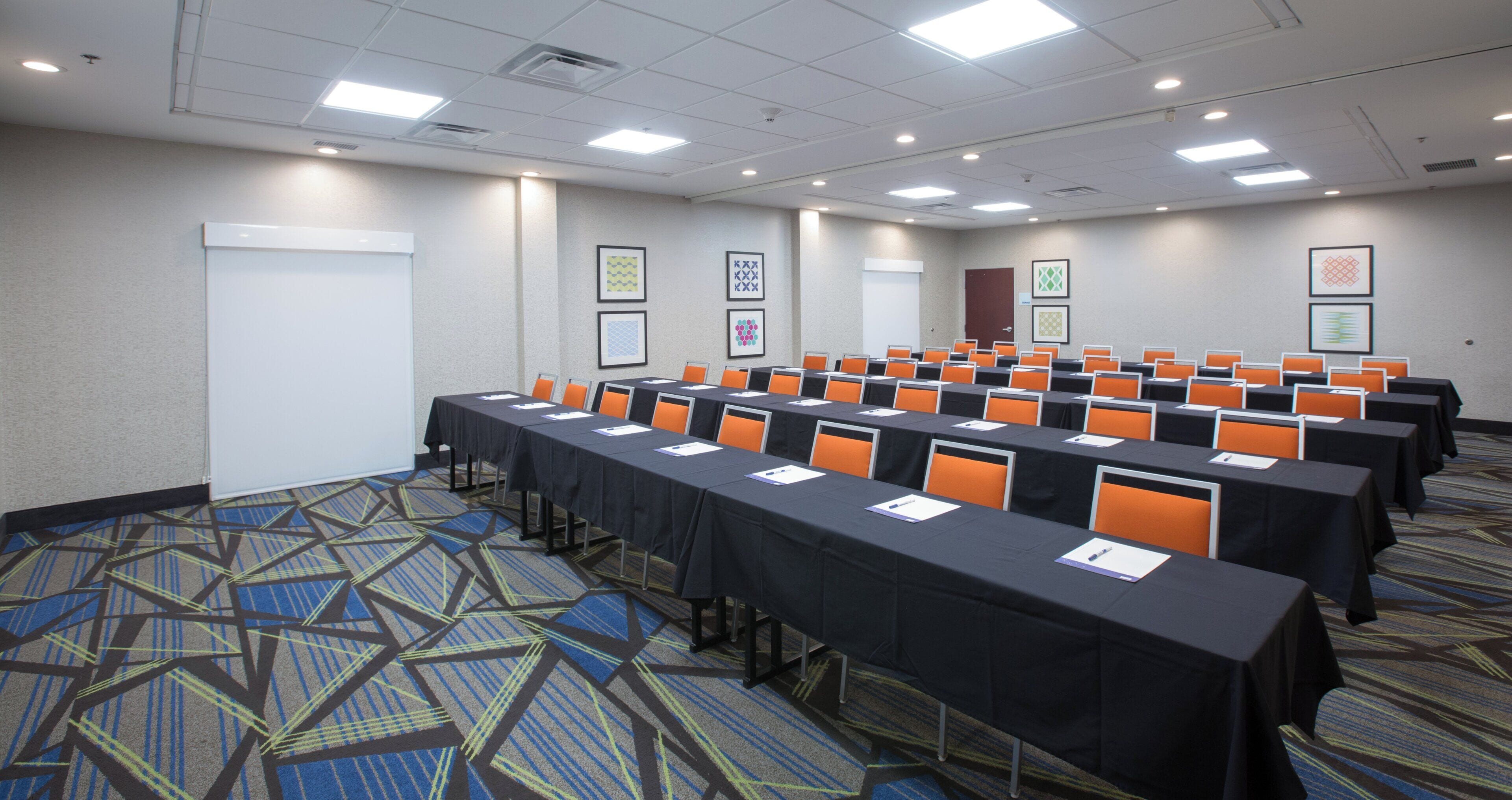 A conference room with rows of tables, chairs, and presentation screens.