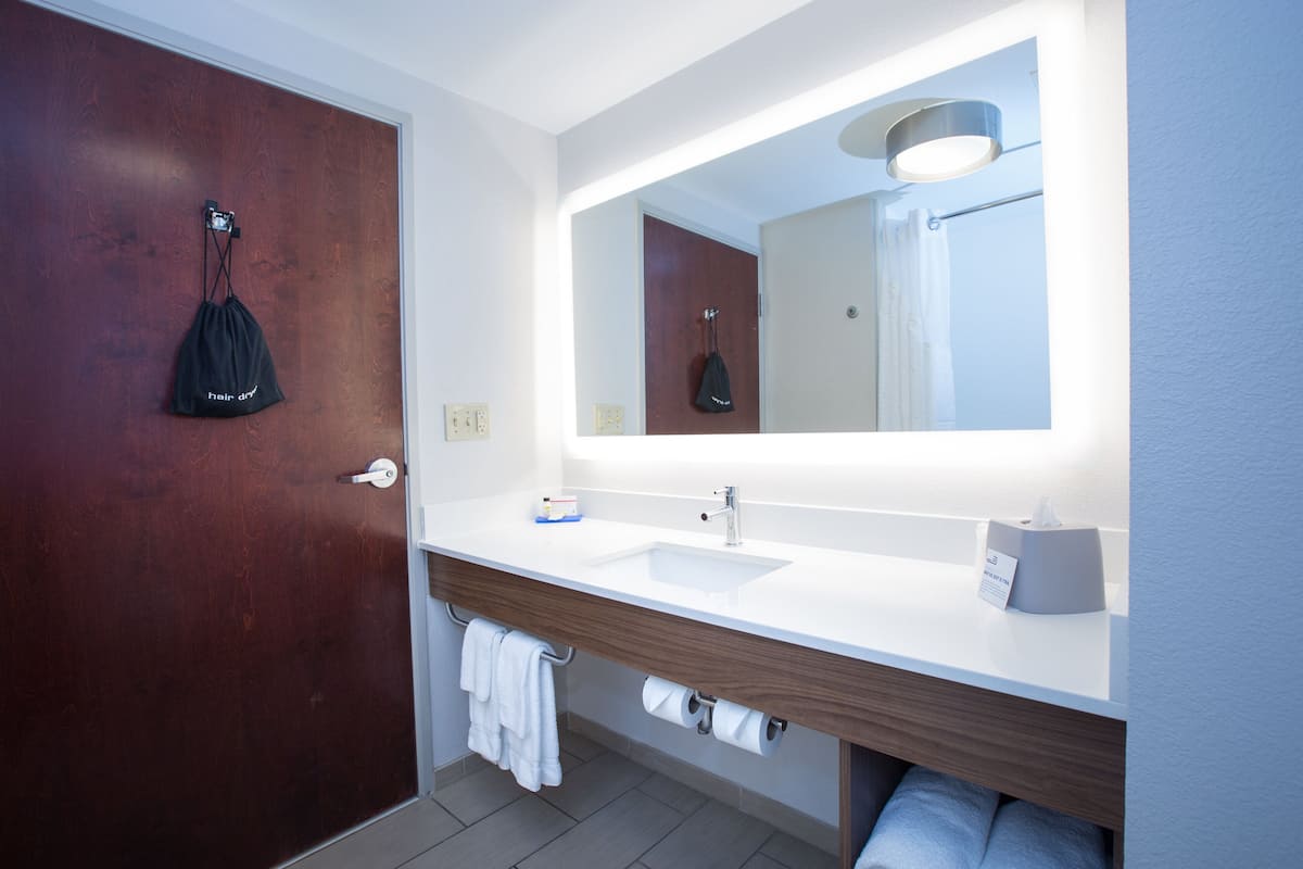 A modern bathroom with a wooden door, a white sink, a mirror, and a towel rack.