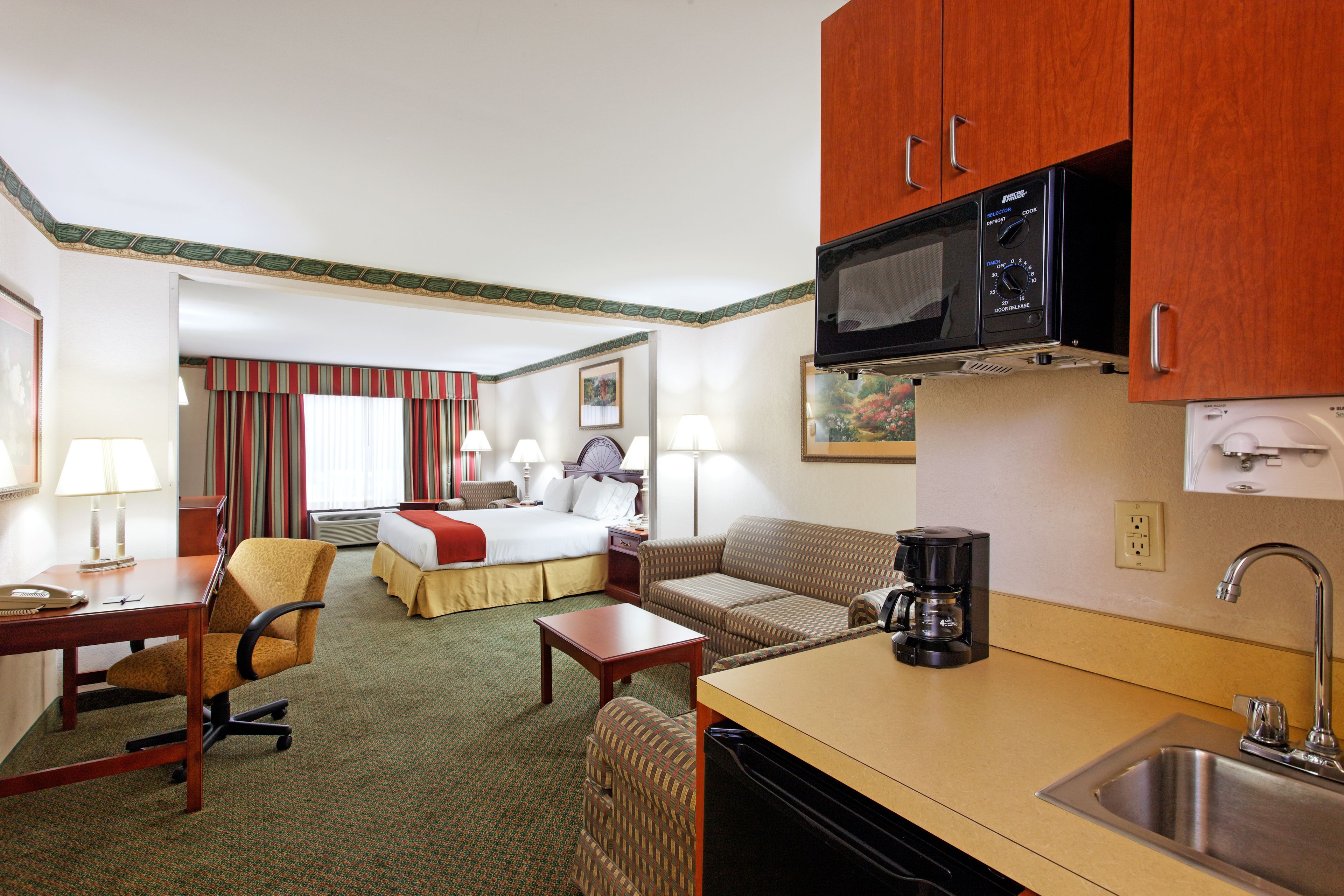 Quarto de hotel com cozinha compacta, cama, sofá, escrivaninha e cafeteira.