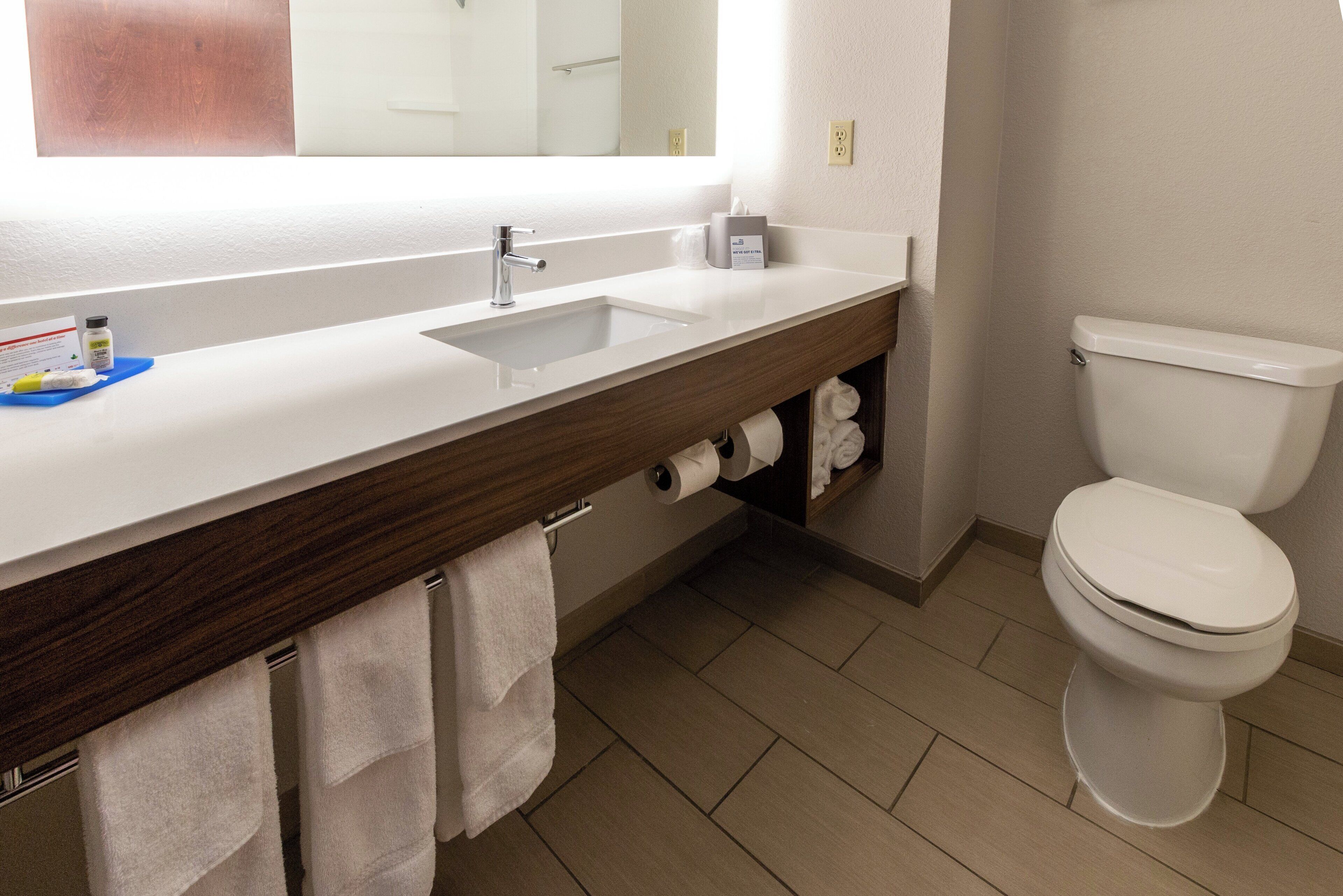 Un baño con lavamanos blanco, espejo, inodoro y toallero.
