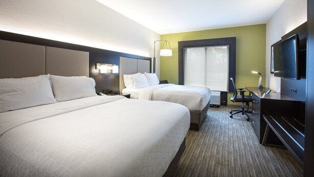 A hotel room with two beds, a desk, a chair, a television, and a window.