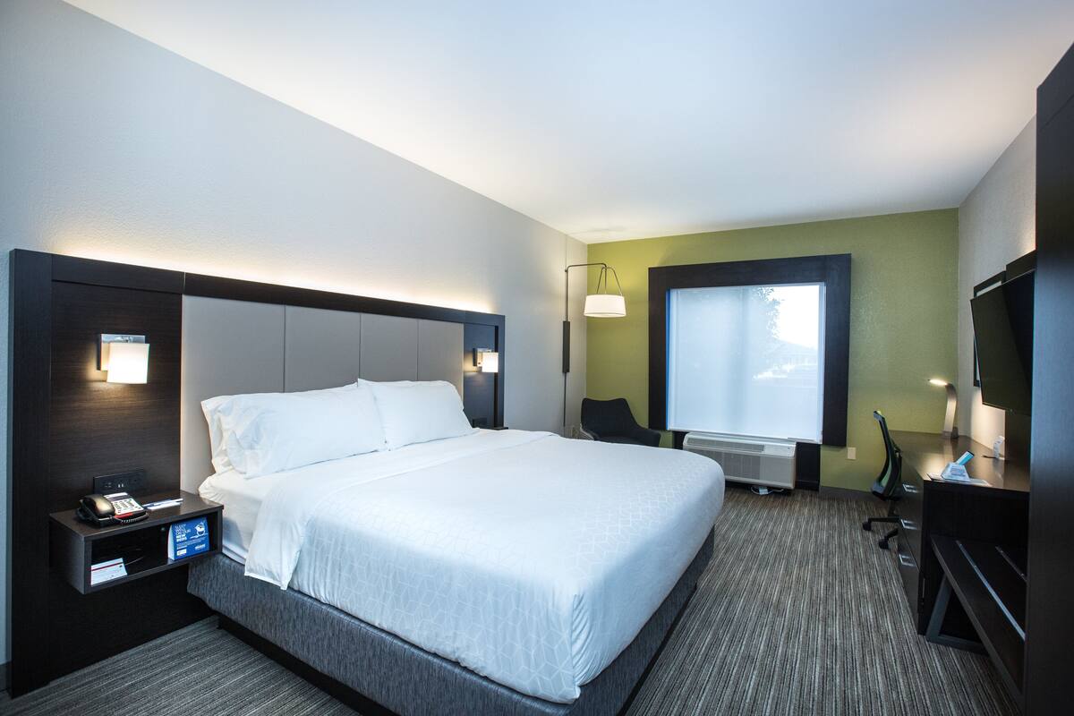 A hotel room with a large bed, a desk with a computer, a chair, a TV, and a window.