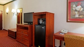 A hotel room with a wooden desk, a black refrigerator, a television, a microwave, a telephone, and a painting on the wall.