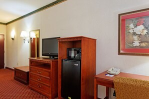 Una camera d'albergo con una scrivania in legno, un frigorifero nero, una televisione, un forno a microonde, un telefono e un quadro appeso al muro.