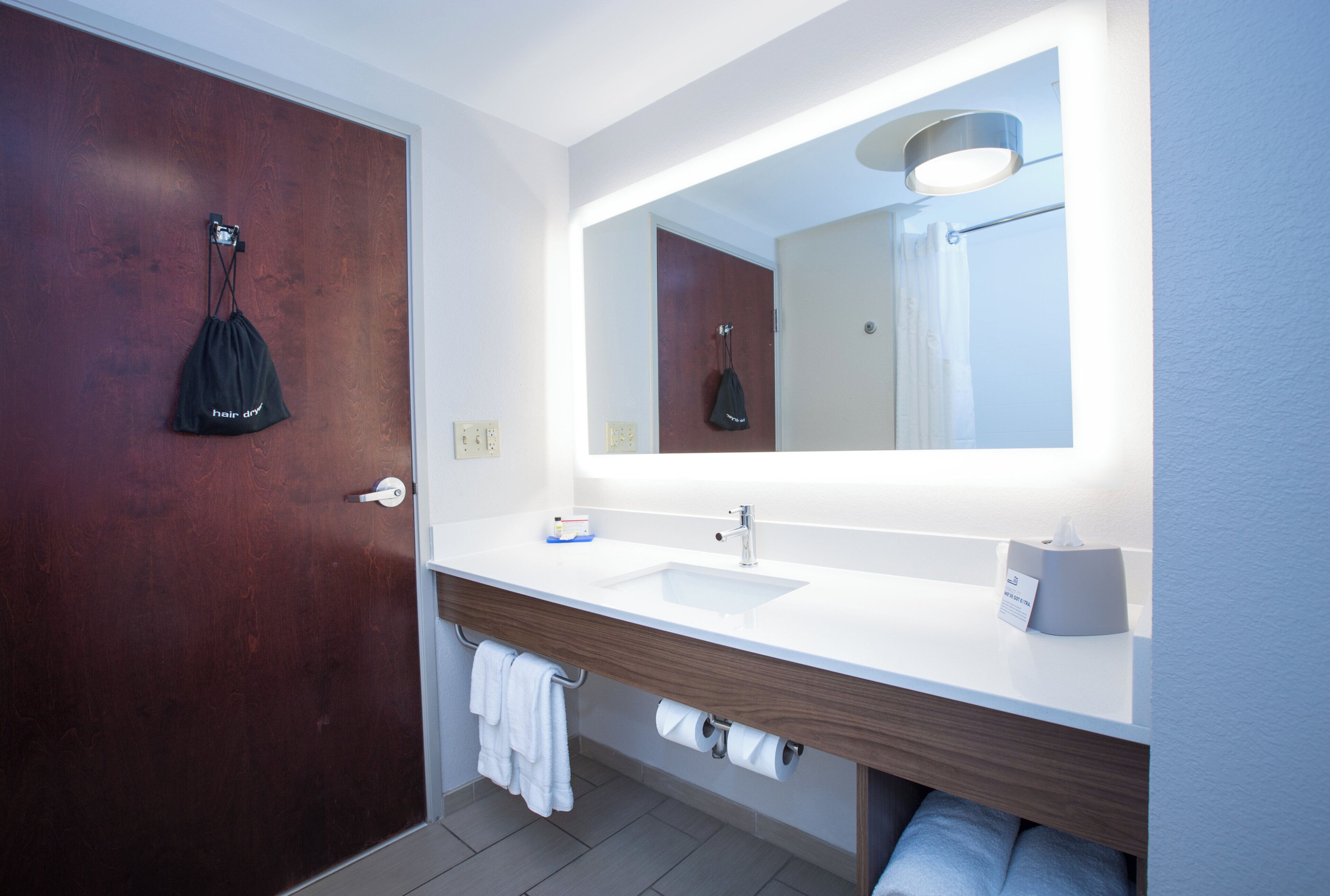 Un baño moderno con puerta de madera, un lavabo blanco, un espejo y un perchero para toallas.