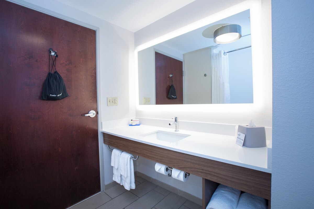 Un bagno moderno con una porta in legno, un lavandino bianco, uno specchio e un porta asciugamani.