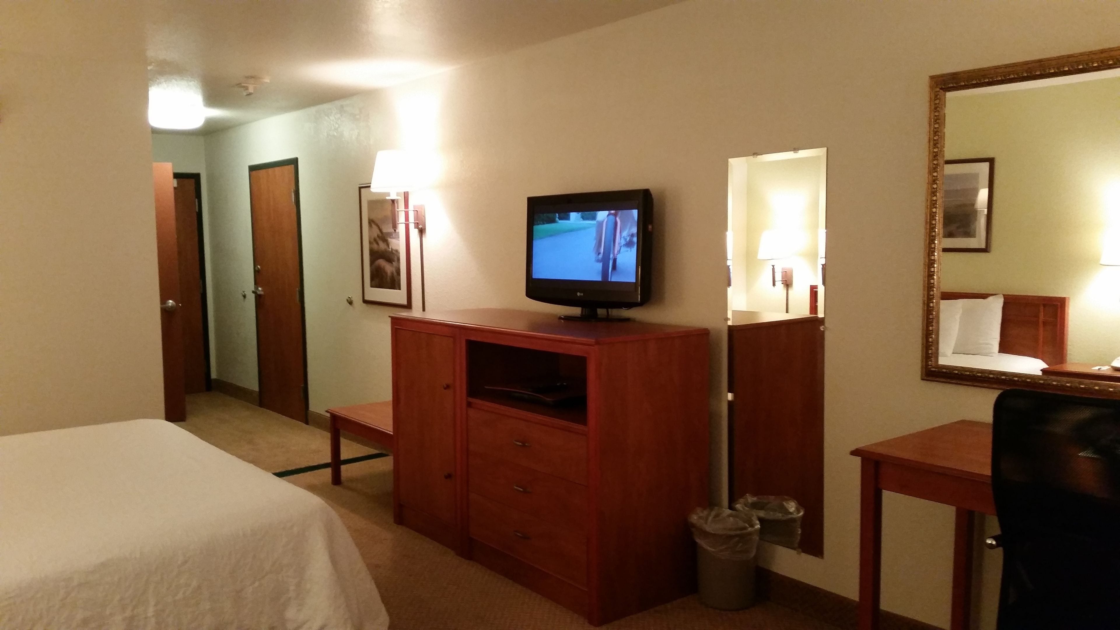 Ein Hotelzimmer mit einem Bett, einem Holzschrank, einem Fernseher, einem Spiegel und einem Mülleimer.