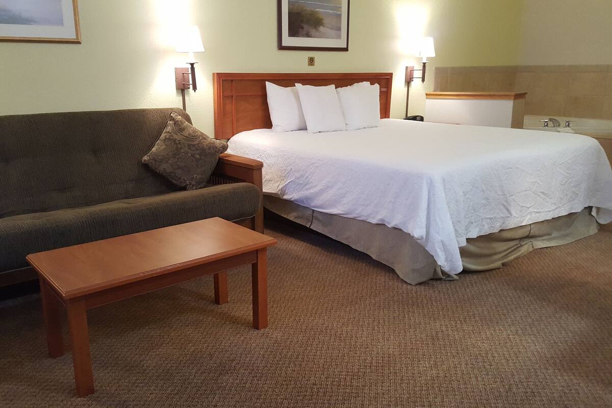 A hotel room with a bed, a sofa, a small table, and two wall-mounted lamps.