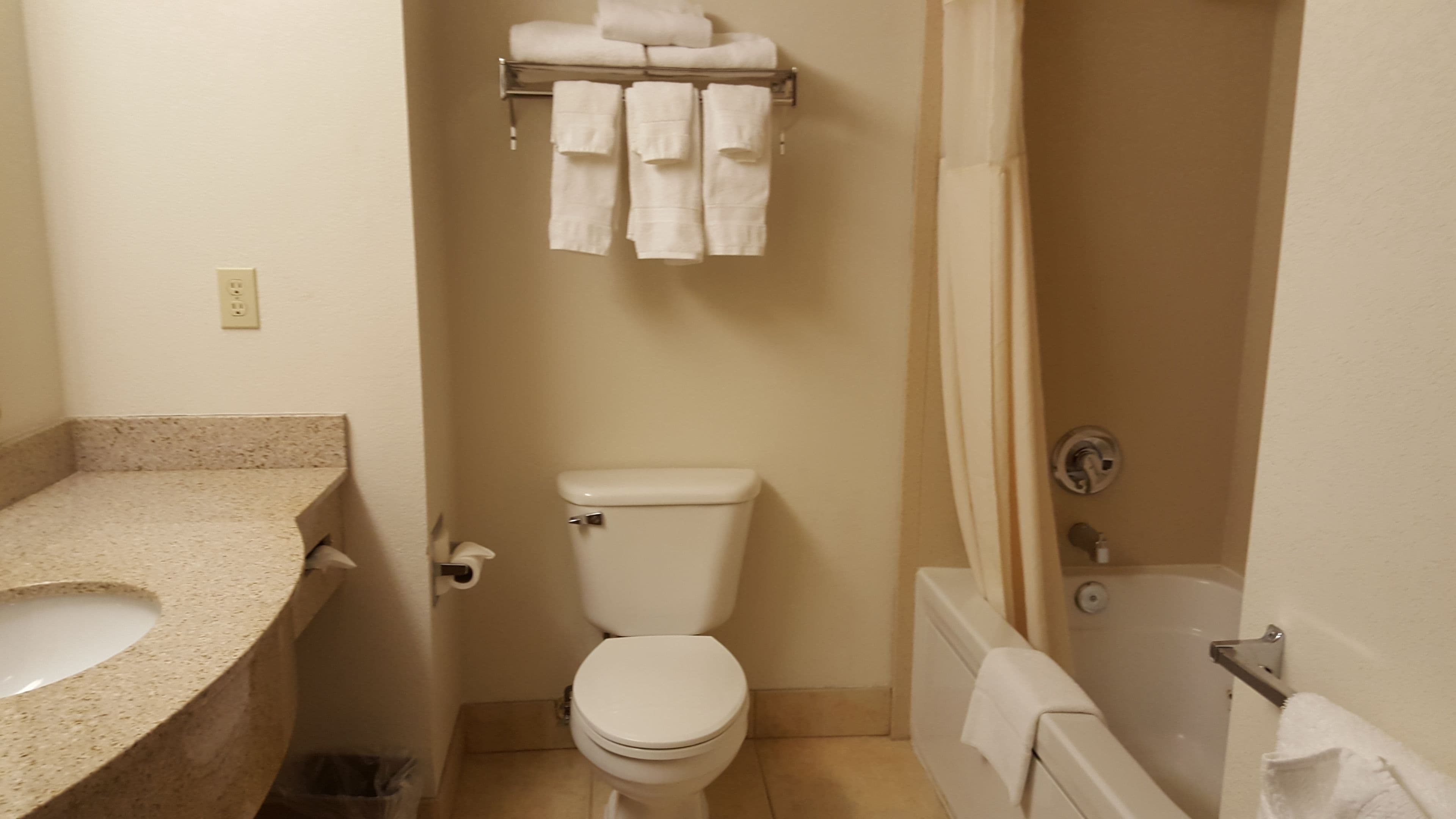 A bathroom with a toilet, sink, and bathtub. There are towels hanging on a rack above the toilet.