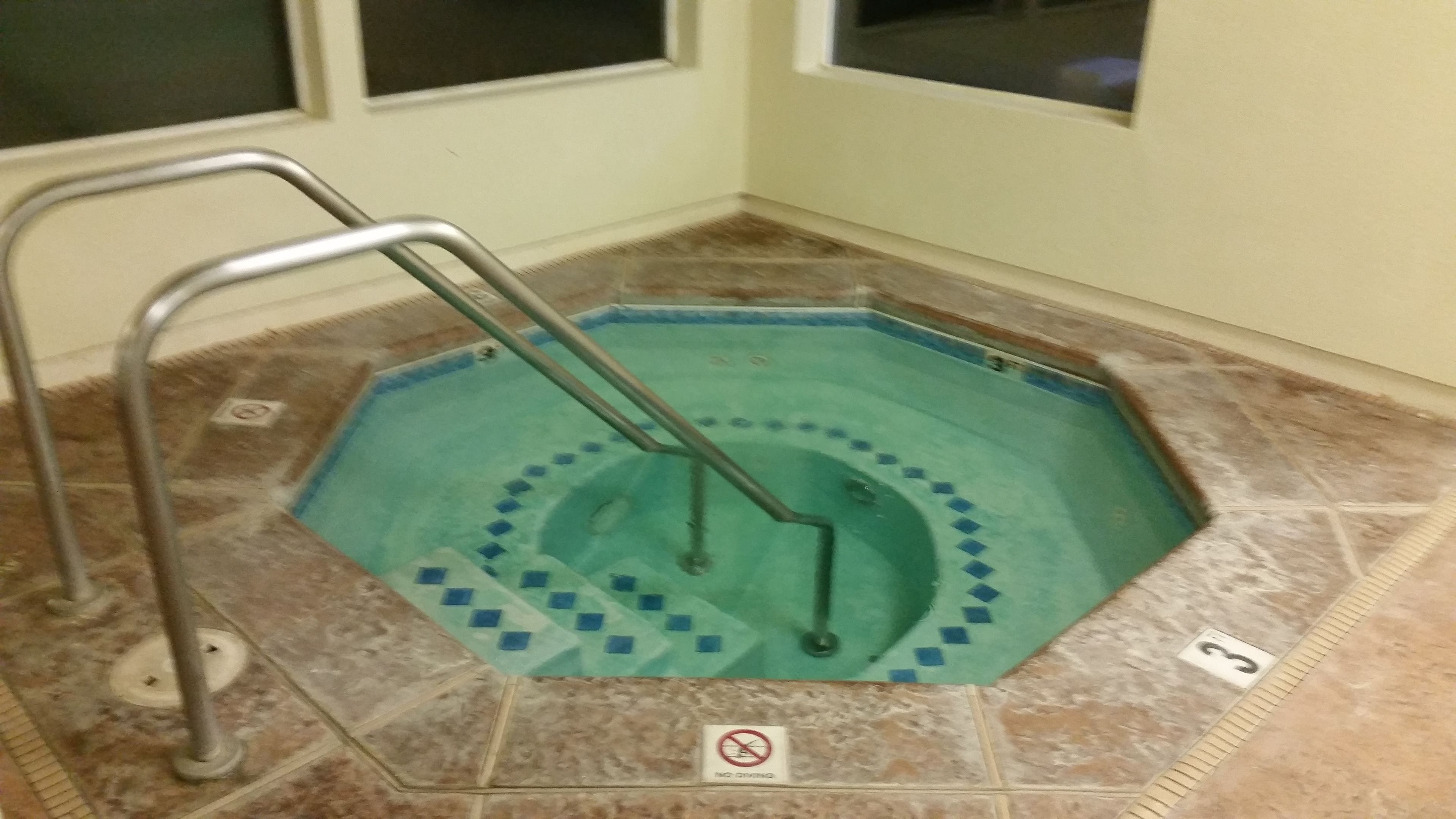 A hot tub with a metal ladder, surrounded by tiled flooring, and a 'No Smoking' sign on the floor.