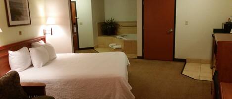 Una habitación de hotel con cama, escritorio, silla, baño con bañera y puerta.