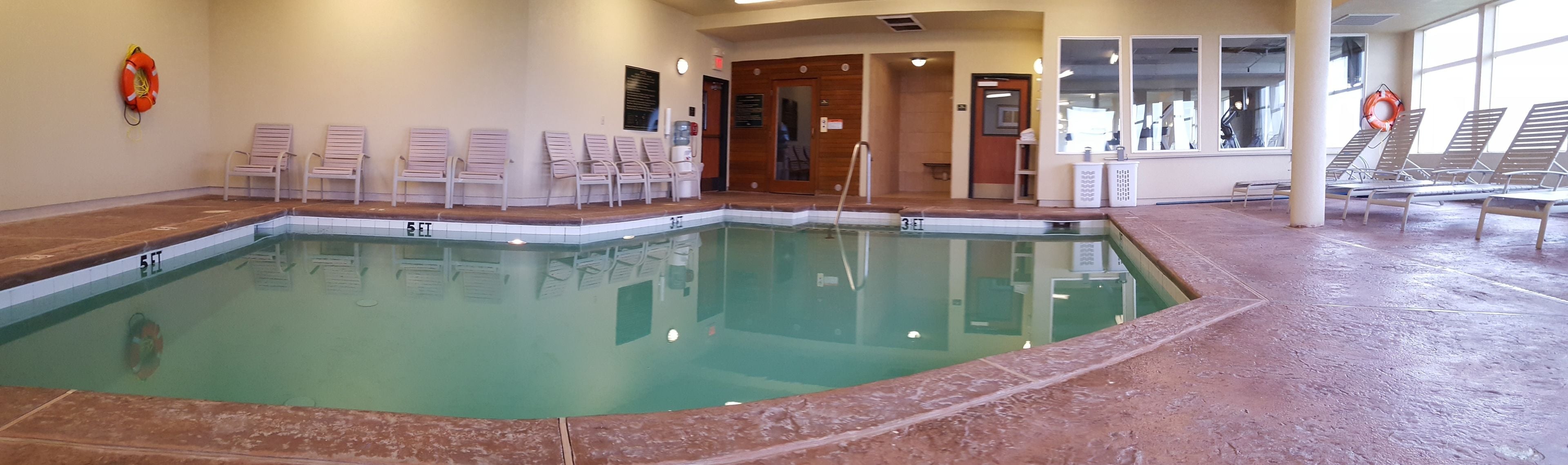 An indoor swimming pool with clear water, marked depth levels, and lounge chairs along the sides.