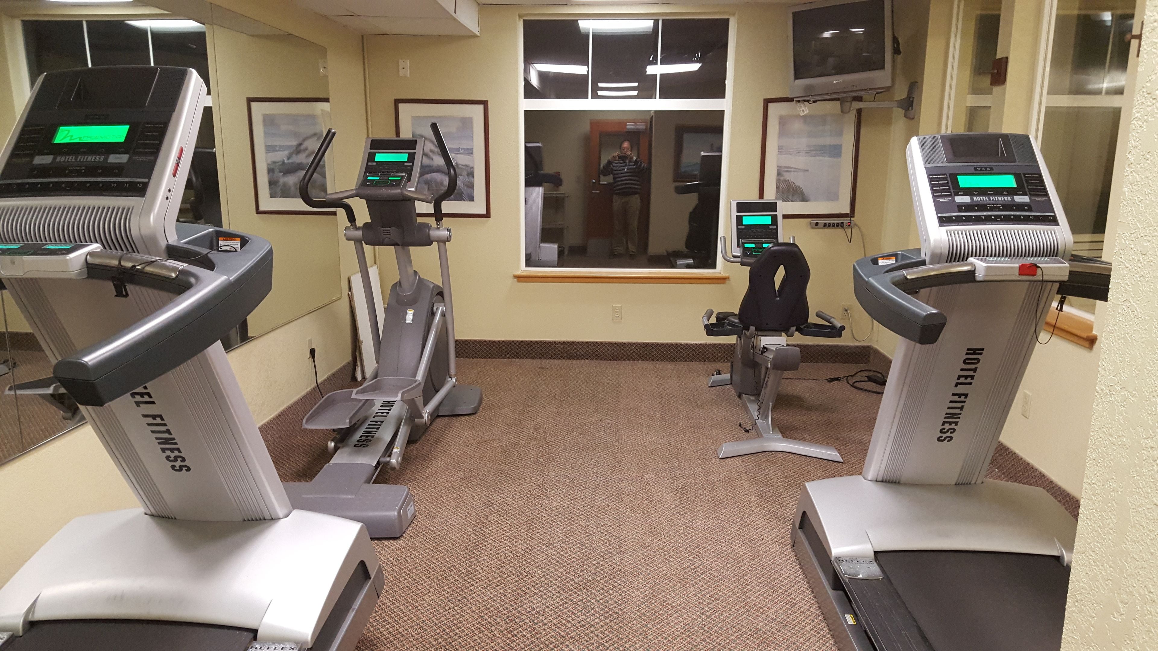 Un gimnasio hotelero con cintas de correr, una elíptica y una bicicleta estática.