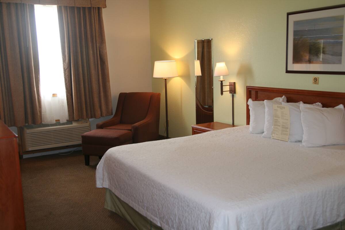 A hotel room with a large bed, a chair, a desk, and a lamp.