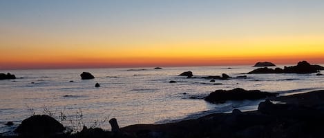 A coastal sunset with rocky outcrops and calm sea.