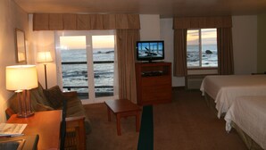 A hotel room with a bed, a desk with a lamp, a television, and a view of the ocean.