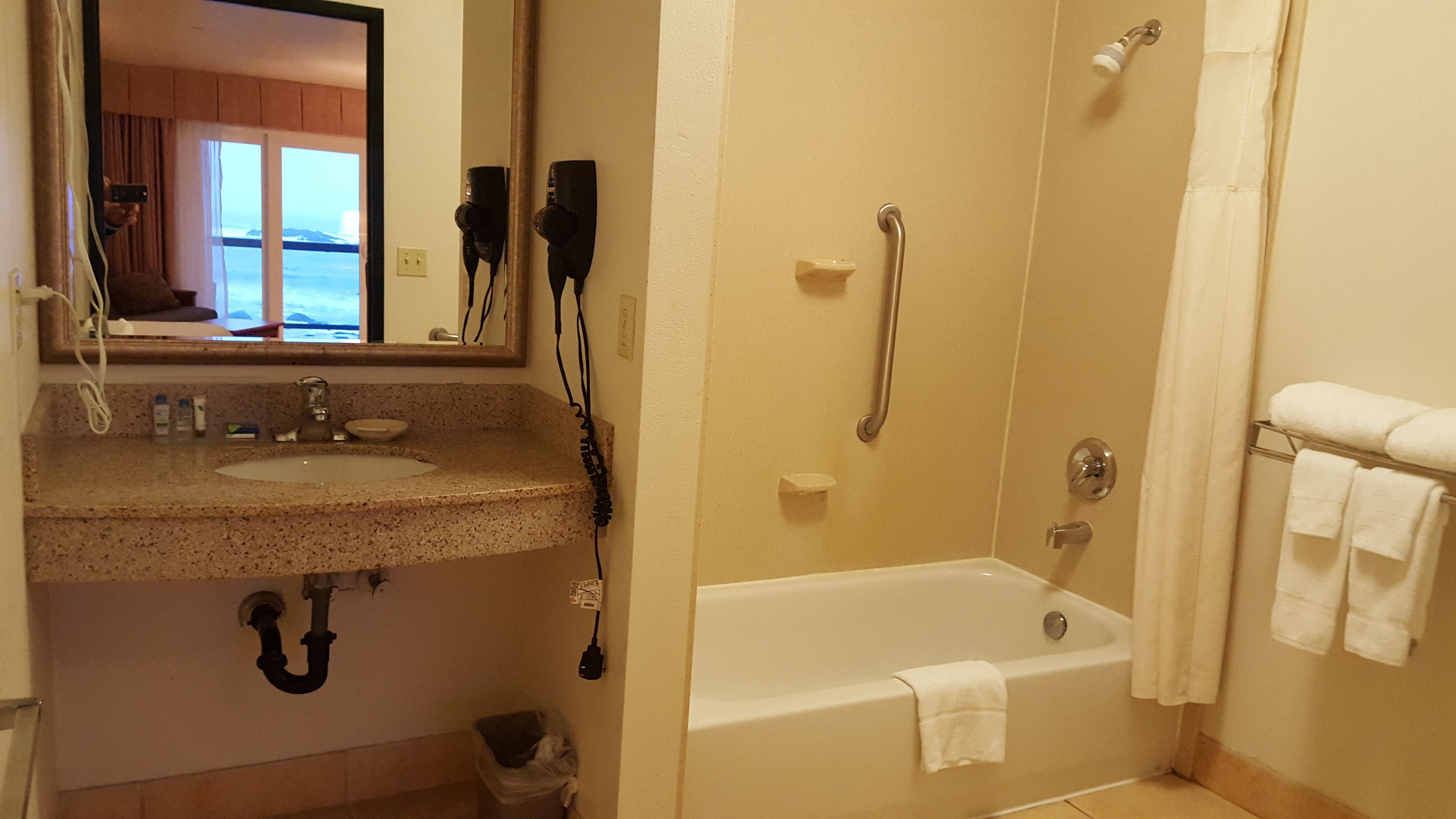 Un baño con lavabo, espejo, secador de pelo y ducha a ras de suelo.