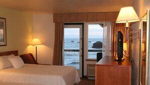 A hotel room with two beds, a desk with a computer, a lamp, and a view of the ocean through a door.