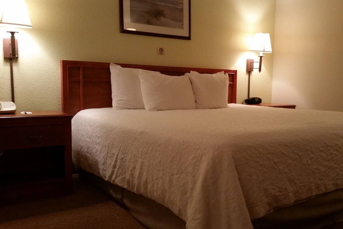 A neatly made bed with white linens, two bedside tables with lamps, and a framed picture on the wall.
