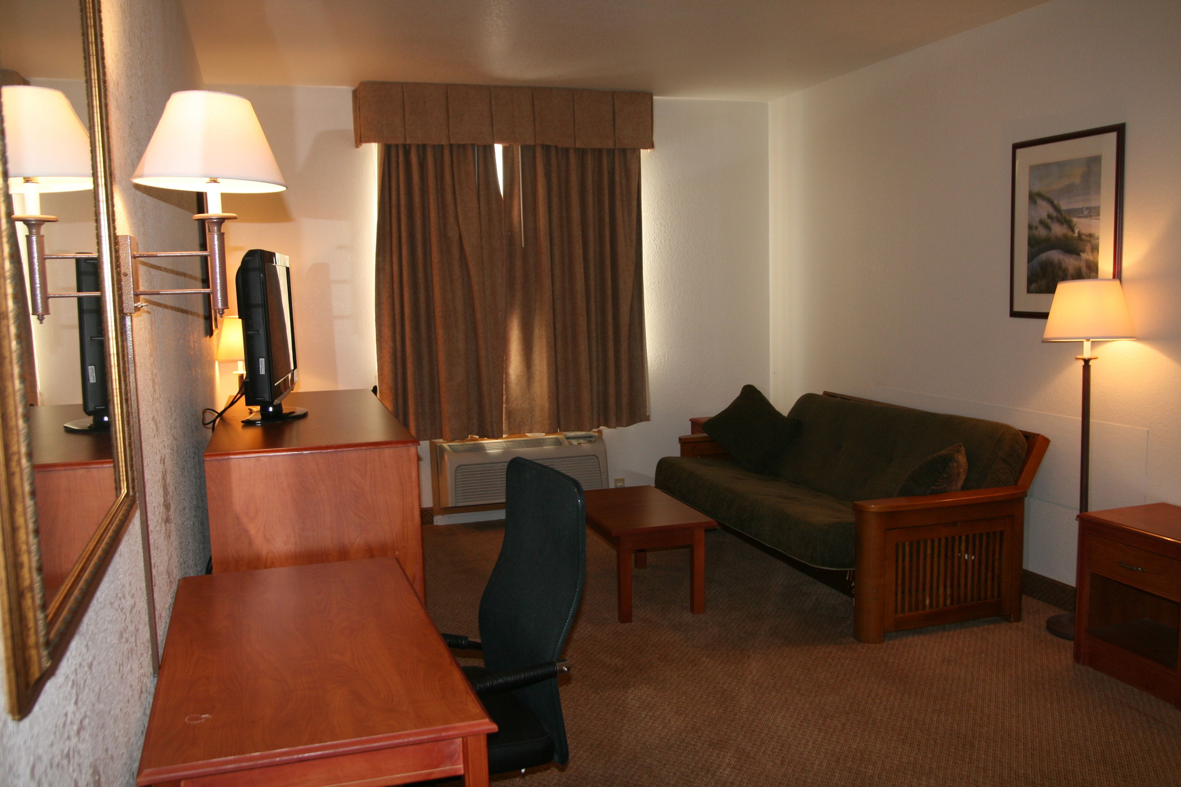 A hotel room with a wooden desk, a green sofa, a small table, a chair, a television, and a lamp.