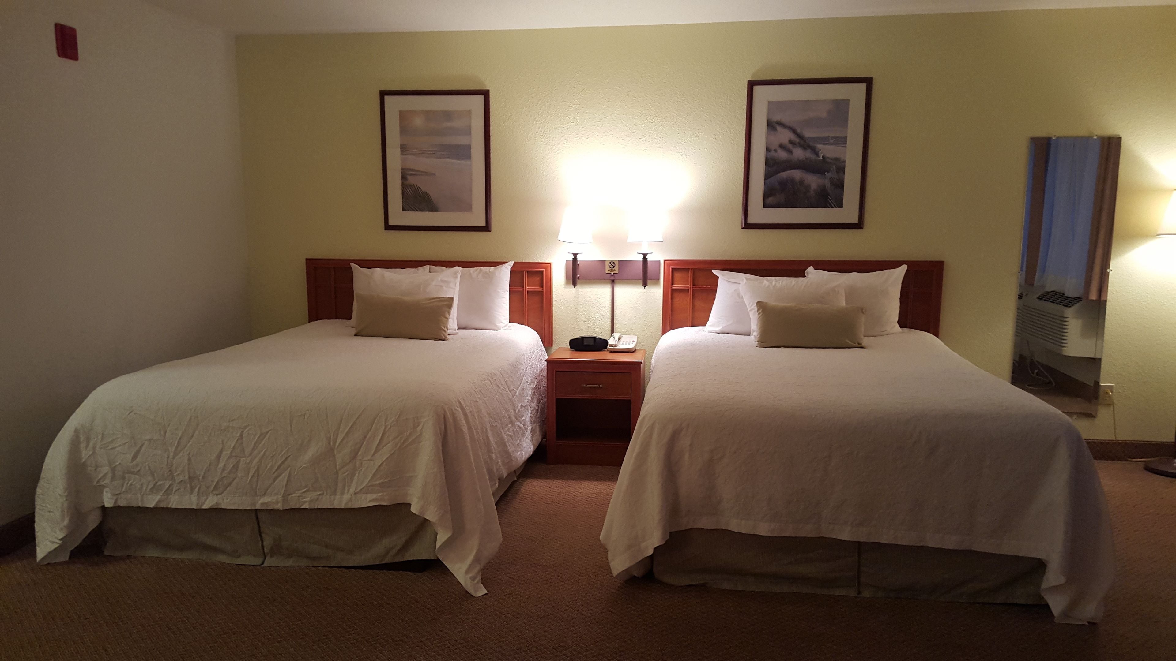Ein Hotelzimmer mit zwei Einzelbetten, einem Nachttisch mit Telefon und Lampe sowie zwei gerahmten Bildern an der Wand.