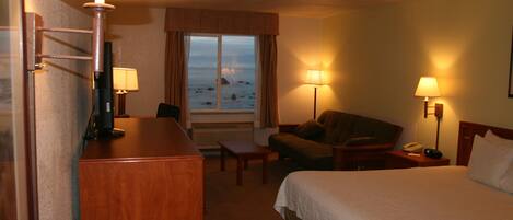 Ett hotellrum med en säng, ett skrivbord, en stol, en soffa och utsikt över stranden.