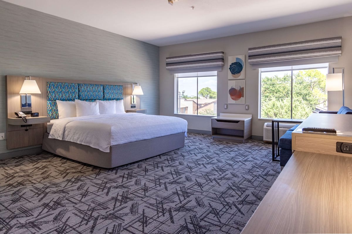 A modern hotel room with a large bed, bedside tables with lamps, a desk, and a view of the outdoors.