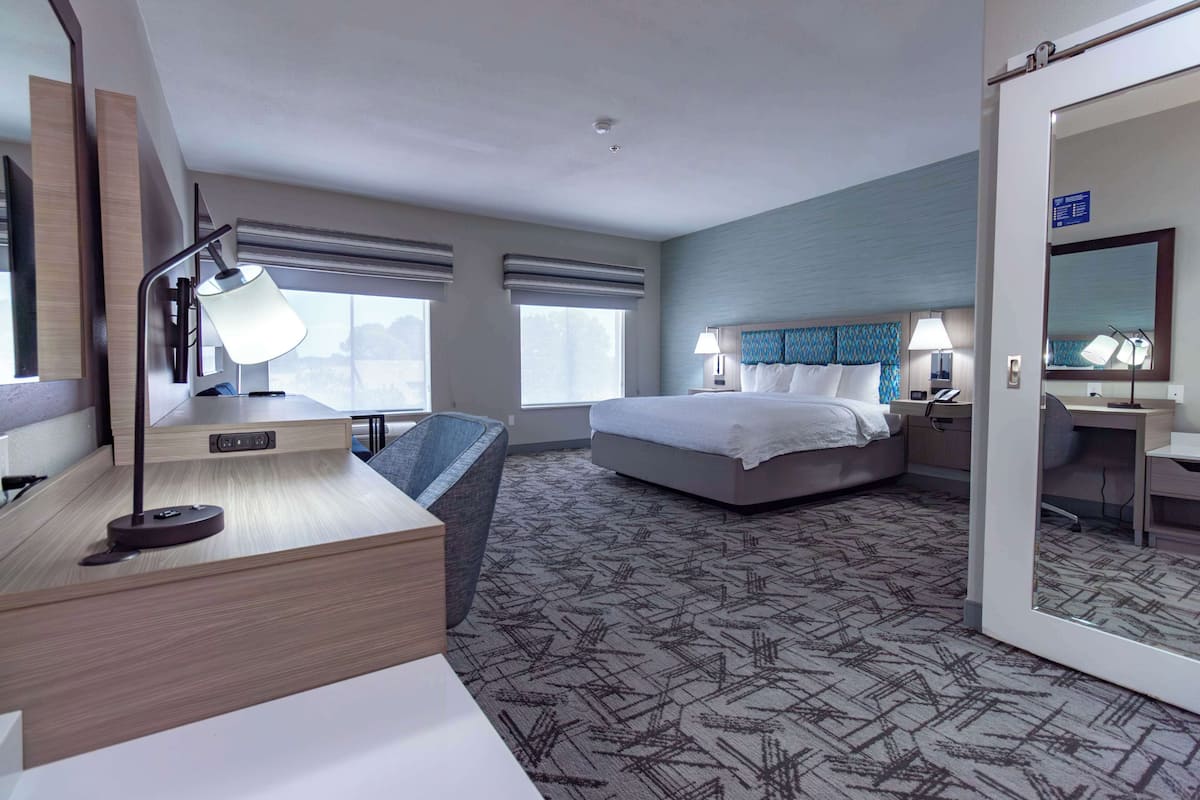 A hotel room with a bed, desk, chair, and large windows.