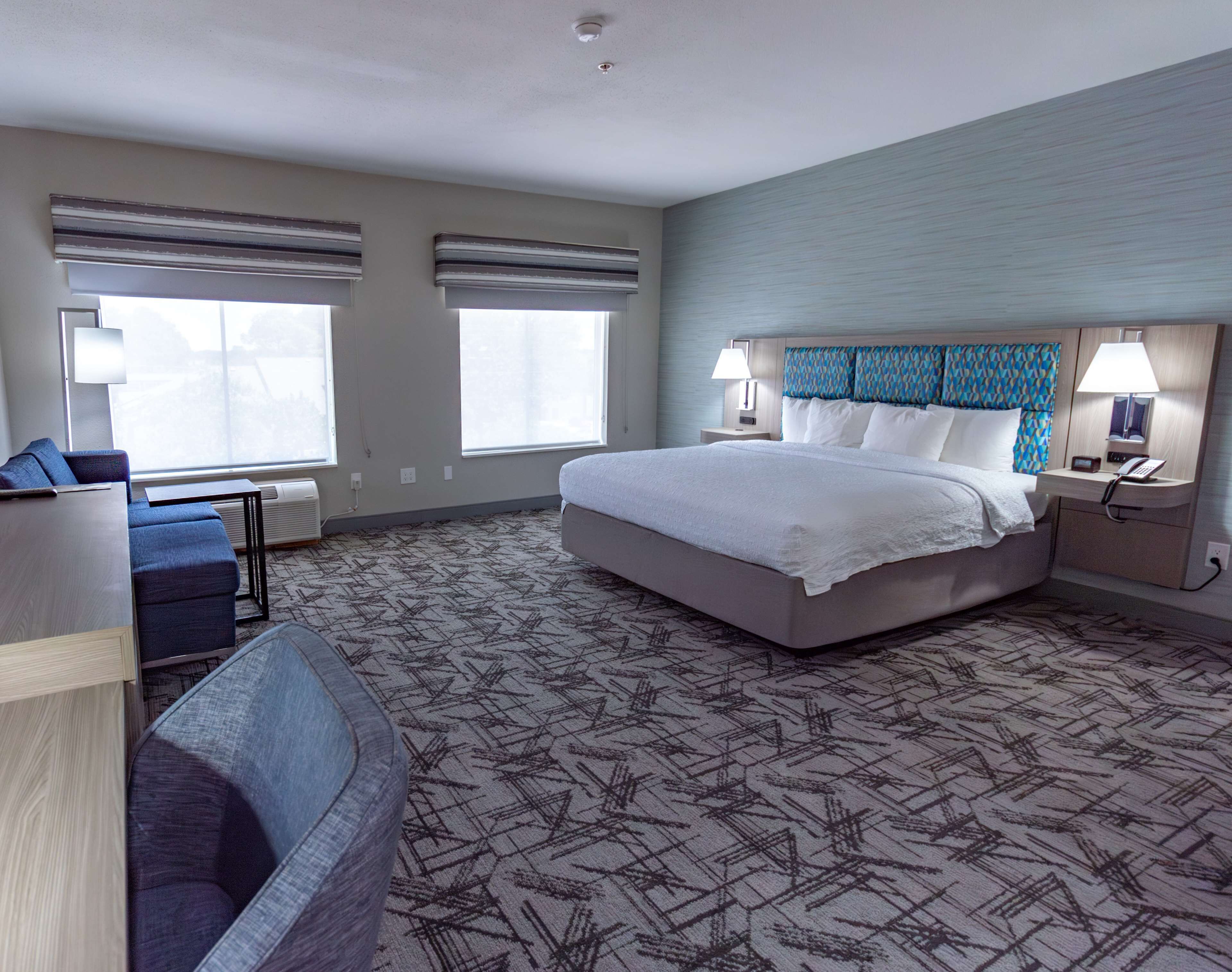 A hotel room with a large bed, two bedside tables with lamps, a sofa, and a desk.