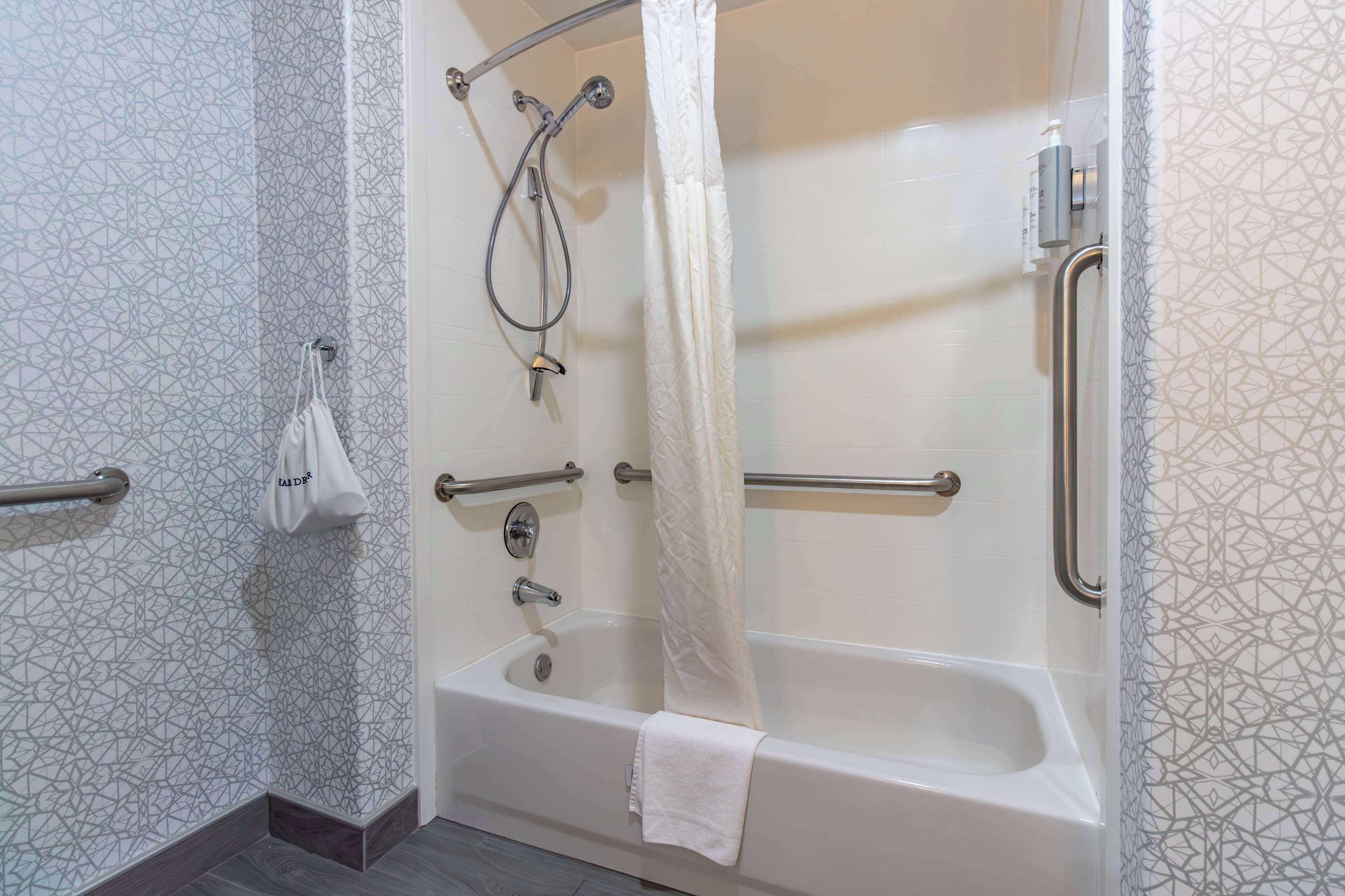 A modern bathroom with a walk-in shower, grab bars, and a towel rack.