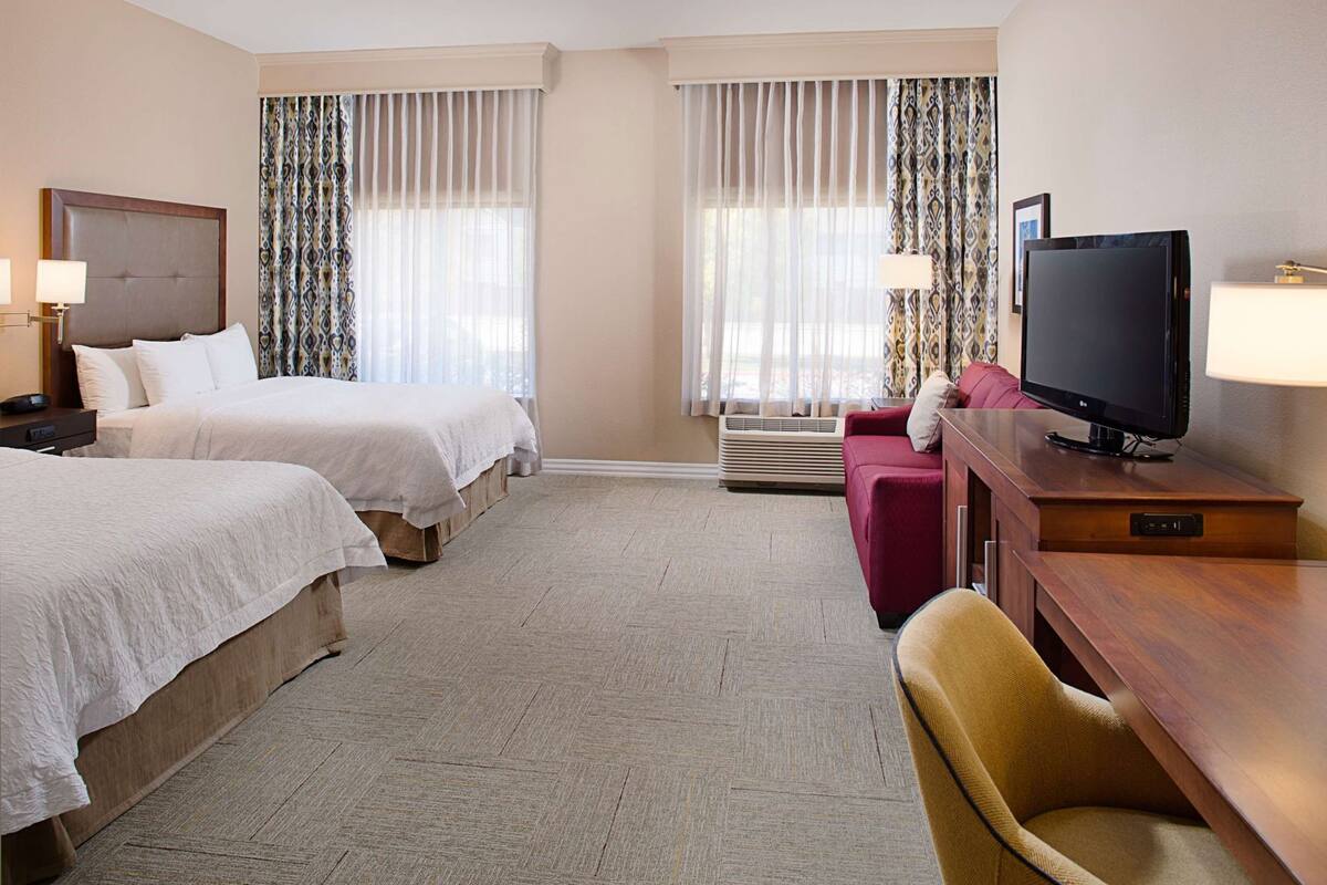 Una habitación de hotel con dos camas, televisión, escritorio y una silla.