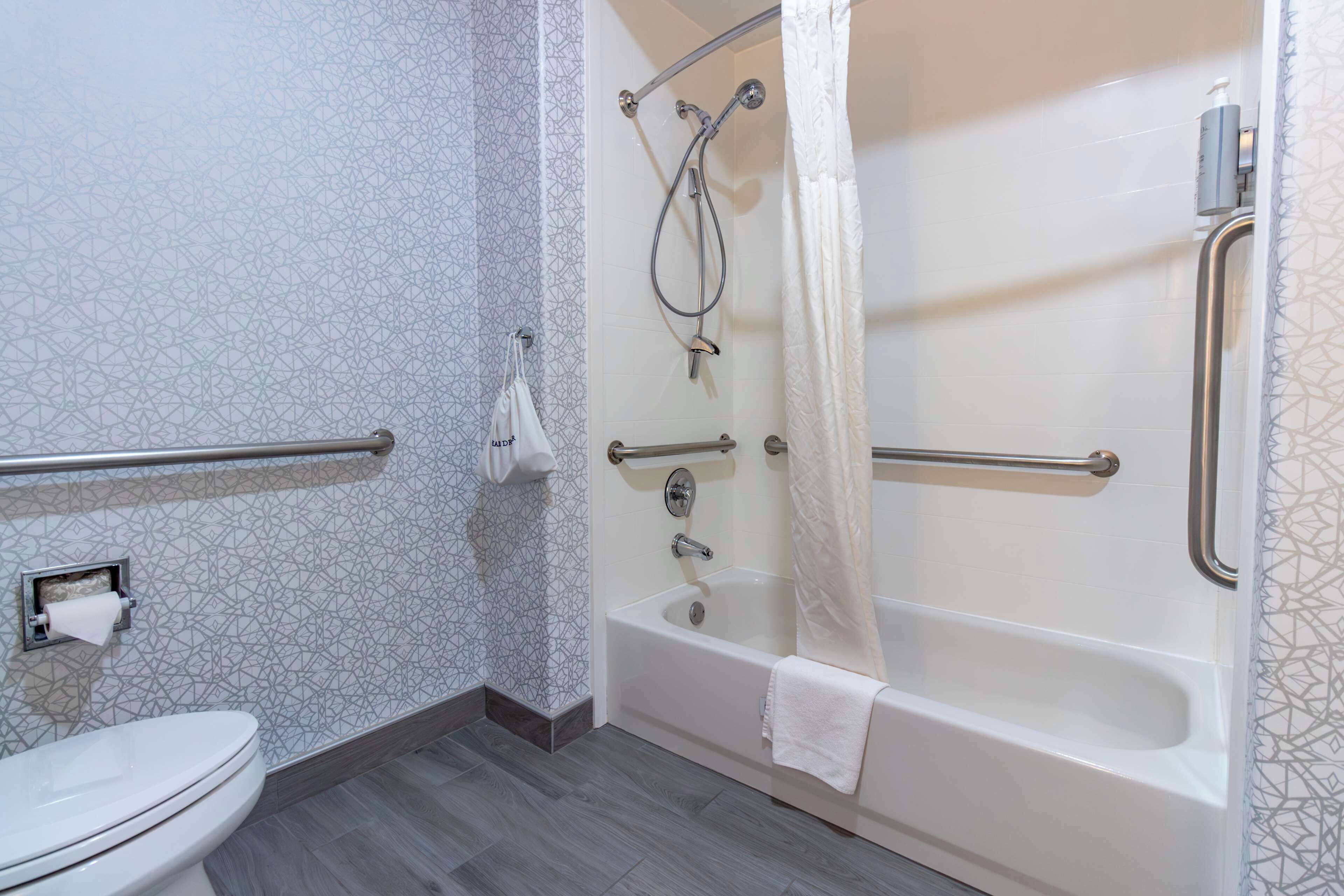 A bathroom with a toilet, a bathtub with a showerhead, and a handrail.
