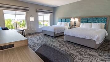 A hotel room with two beds, a desk, and a view of the outside.