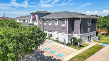 A multi-story hotel with a grey and white exterior, a parking lot with handicapped parking spaces, and a flagpole with an American flag.