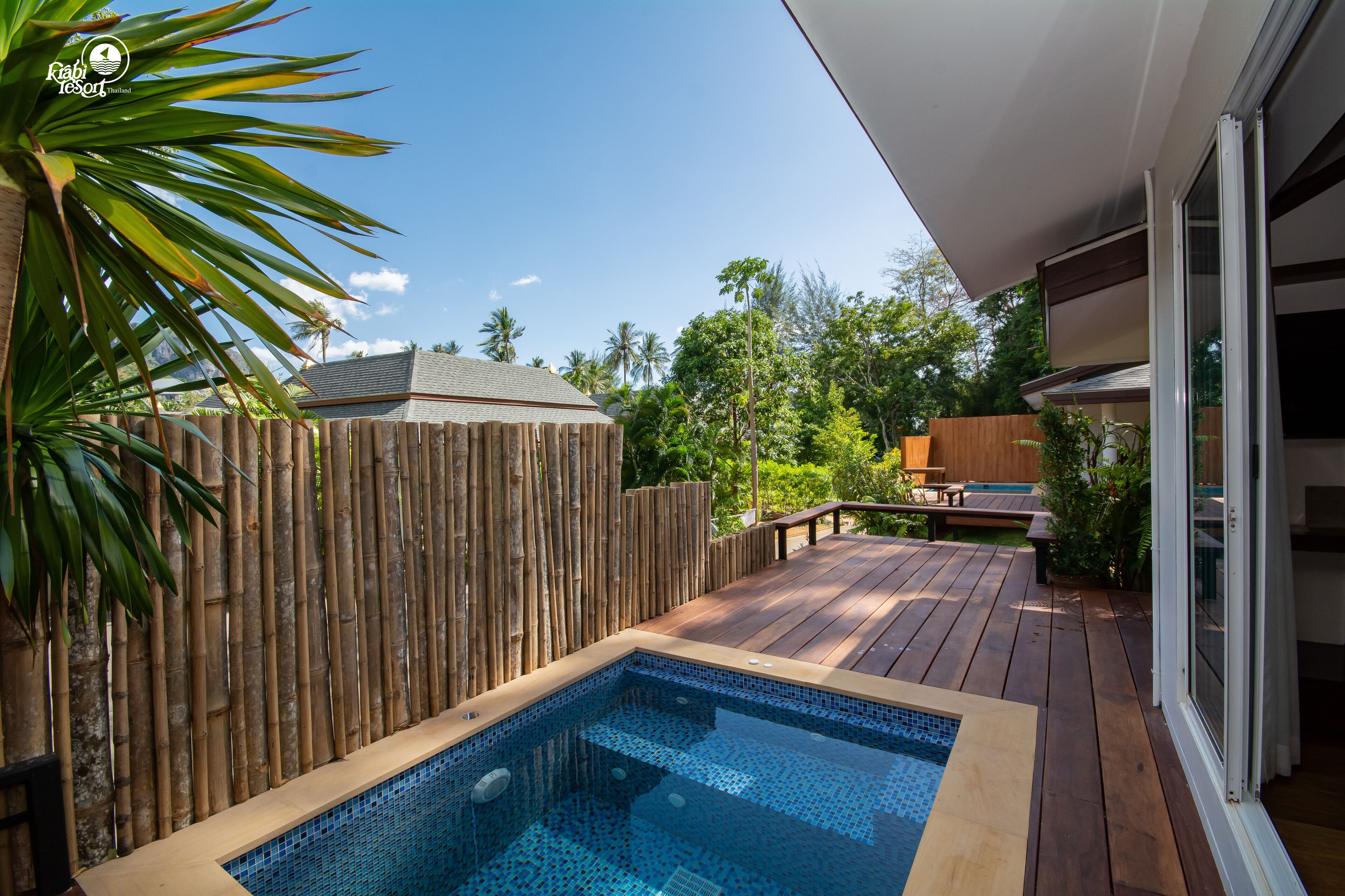A backyard with a wooden deck, a swimming pool, and a bamboo fence.