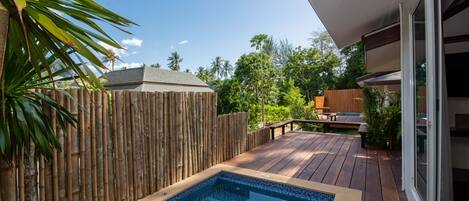 A backyard with a wooden deck, a swimming pool, and a bamboo fence.