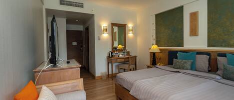 A hotel room with a large bed, a desk with a chair, a television, and a bathroom visible through an open door.