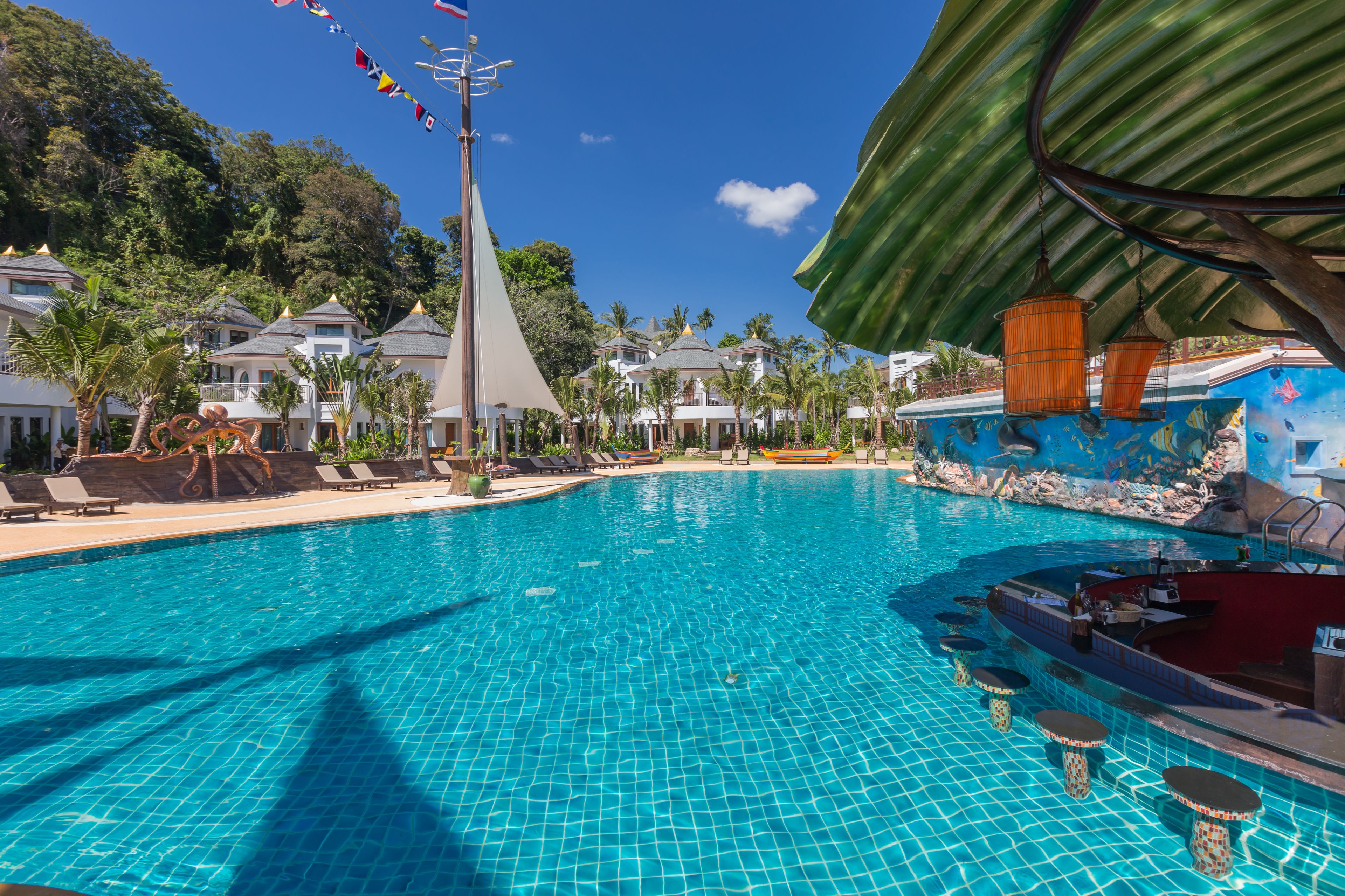 A large swimming pool with a bar area, lounge chairs, and a sail-shaped structure.