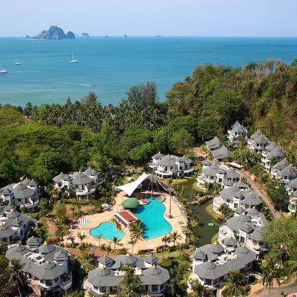 A resort with multiple bungalow-style buildings, a central swimming pool, and a view of the ocean.