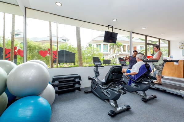 A gym with exercise equipment, large windows, and a view of buildings and trees. - Krabi Resort (Krabi)