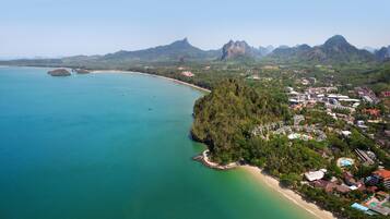 An aerial view of a coastal area with a beach, a forested peninsula, and a town with buildings.