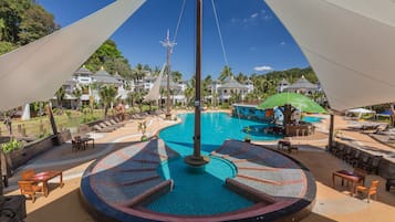 Relax by the central pool surrounded by lounge chairs and tables amidst lush greenery and palm trees.
