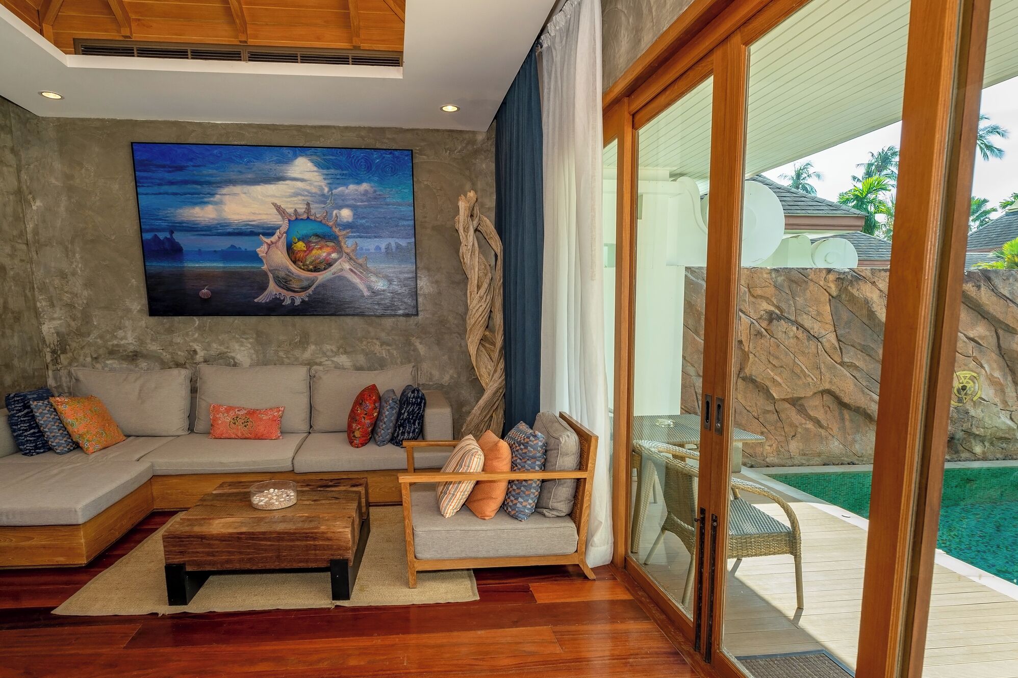 Un soggiorno moderno con un grande quadro, un divano, un tavolino da caffè e vista su una piscina attraverso una porta in vetro.