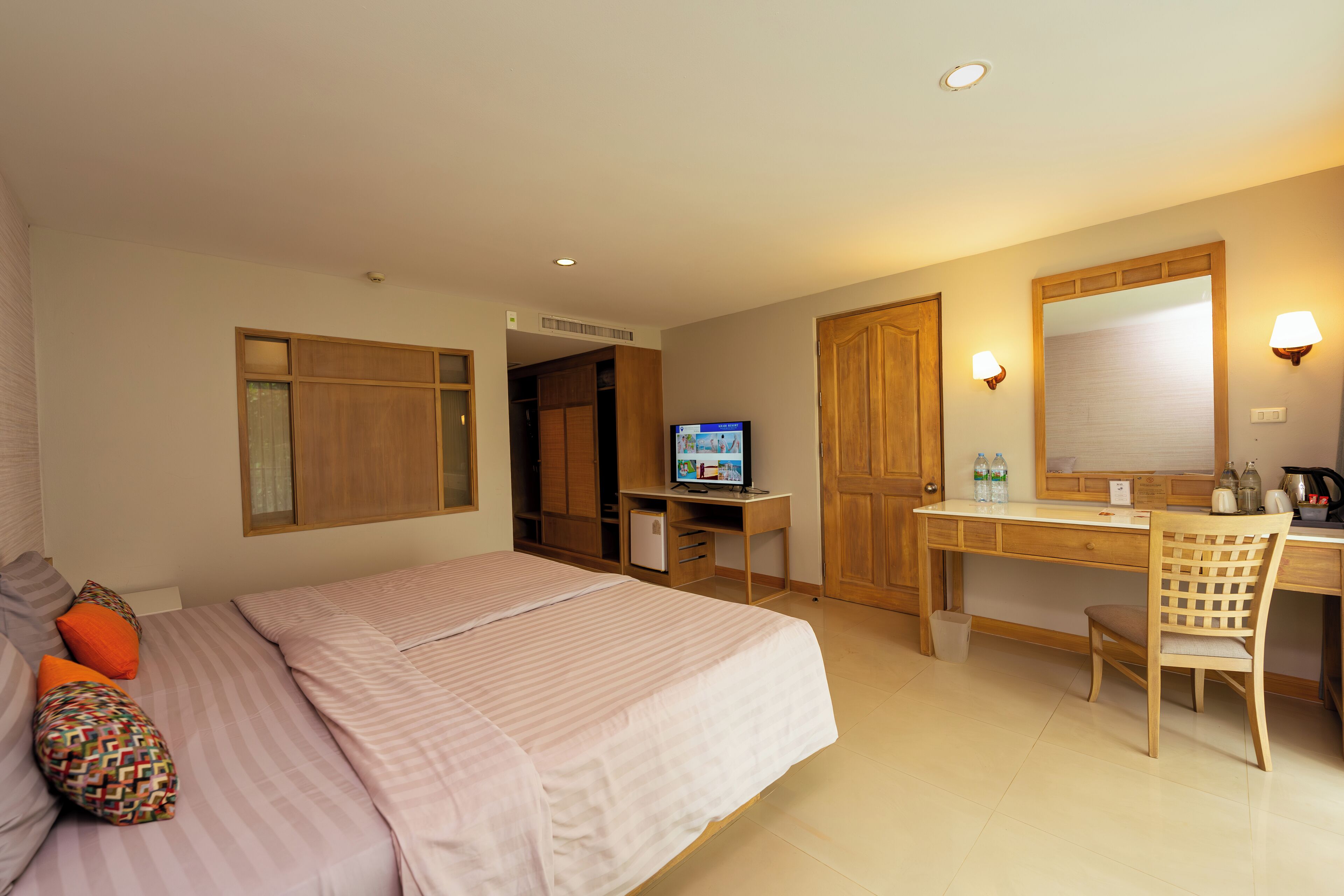 Una camera d'albergo con un letto, una scrivania, una sedia, televisione, armadio e uno specchio.