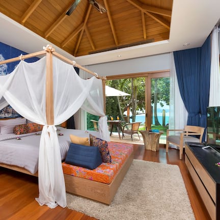 A bedroom with a canopy bed, wooden flooring, a nightstand with a lamp, and a mural on the wall.
