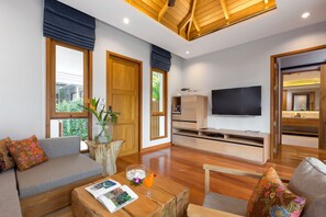 A modern living room with a wooden ceiling, a large TV, and a sofa with colorful cushions.