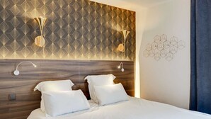 A modern hotel room with a geometric patterned wallpaper, a wooden headboard, two white beds with pillows, and a wall-mounted geometric light fixture. - Hotel Carladez Cambronne (Paris)