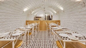 A dining area with white metal chairs and tables, patterned floor tiles, and a brick wall backdrop. - Hotel Carladez Cambronne (Paris)