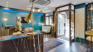 A hotel lobby with a marble reception desk, a chandelier, and a view of the street through a glass door. - Hotel Carladez Cambronne (Paris)